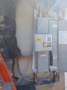 Electrical panel installation with safety labels and wiring components visible.
