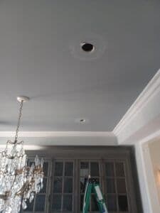 Ceiling during renovation showing recessed light fixture and chandelier. Ladder visible in background.