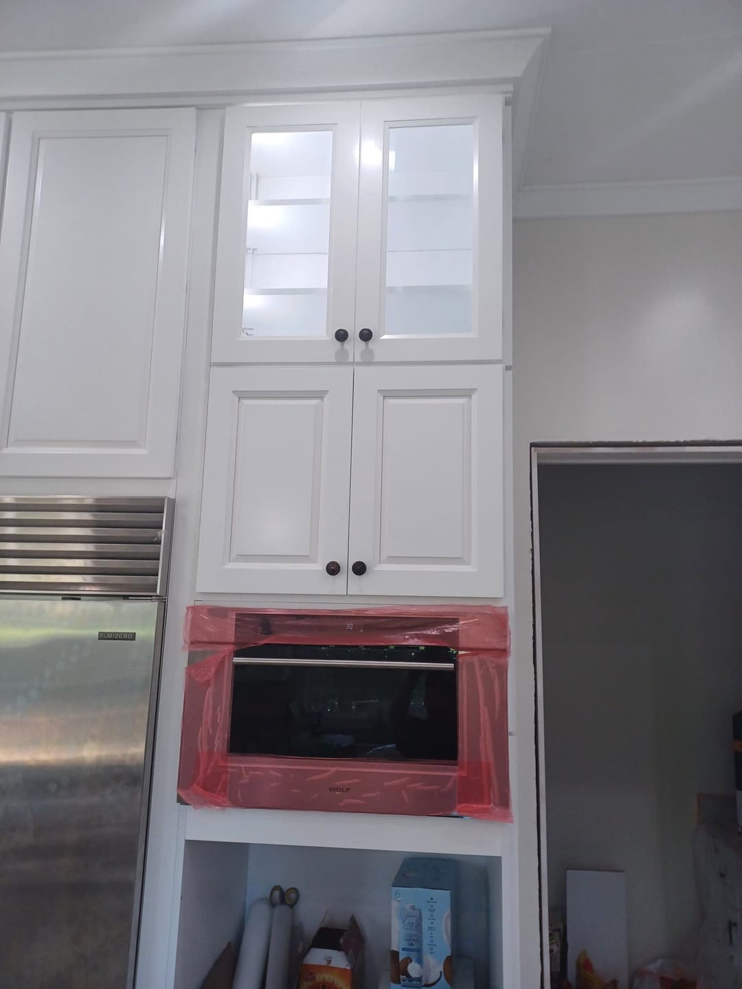 Modern kitchen cabinetry with glass doors above a microwave, featuring sleek white design and black hardware.
