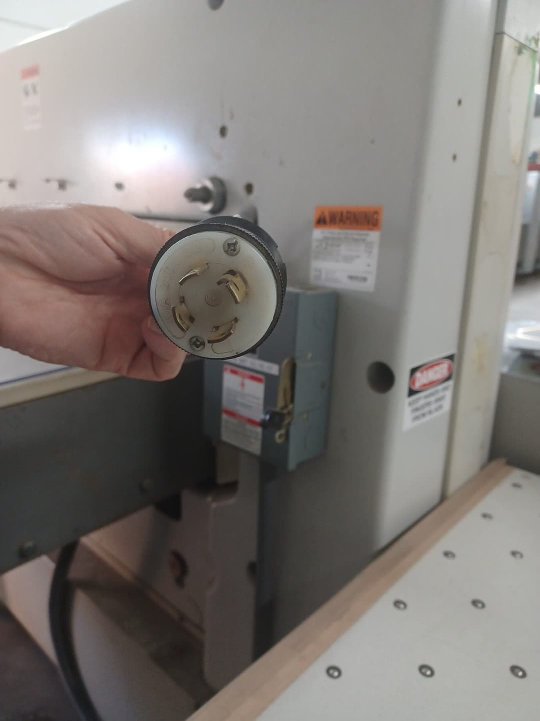 Hand holding a power plug near a large industrial machine in a workshop setting.
