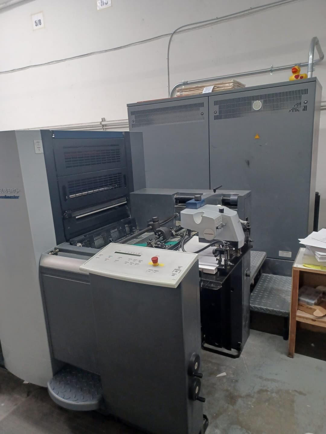 Printing press machine in a workshop, featuring control panel and paper feed system.