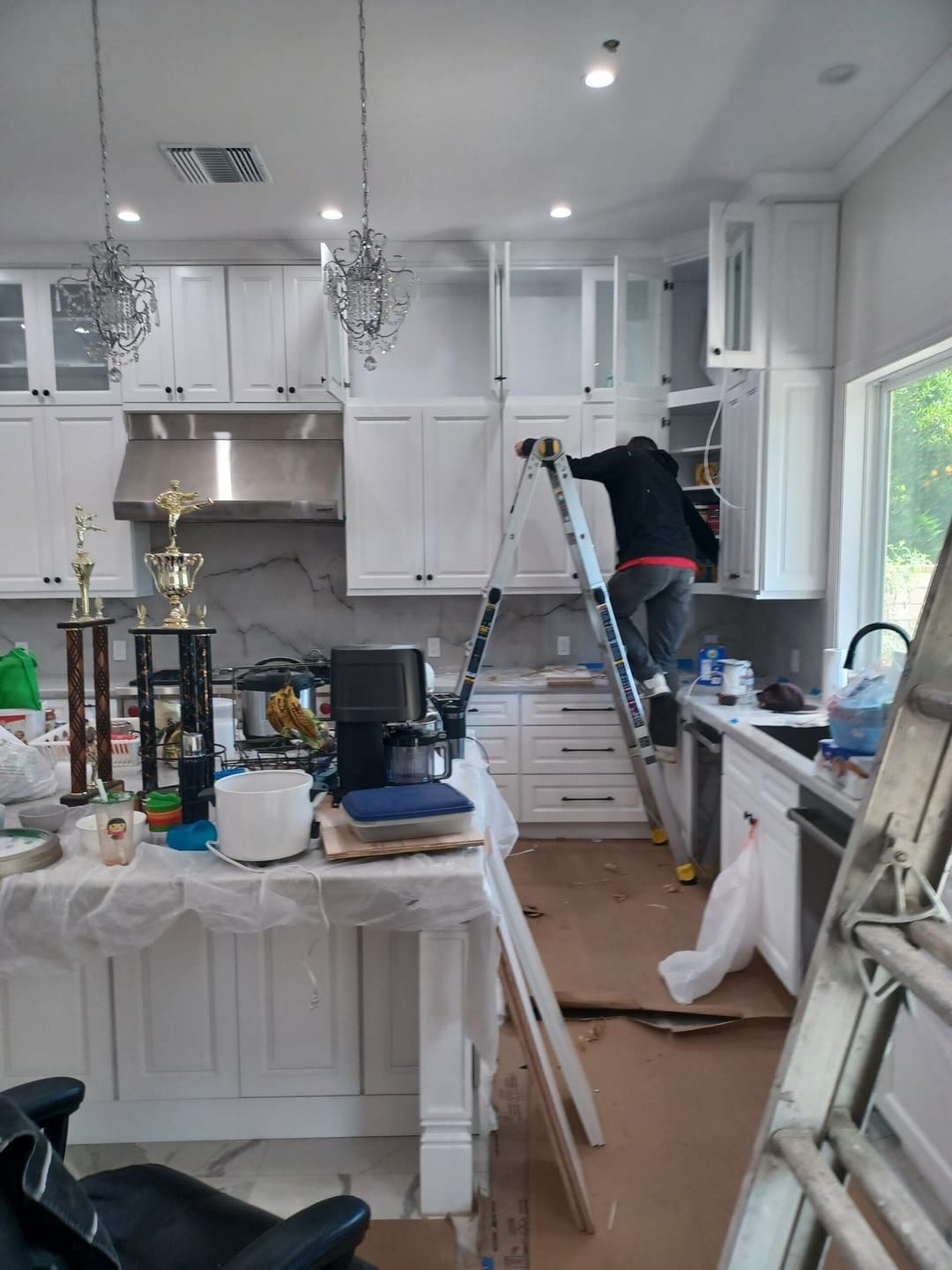 Renovation in progress: worker installing cabinets in modern white kitchen with tools and trophies.